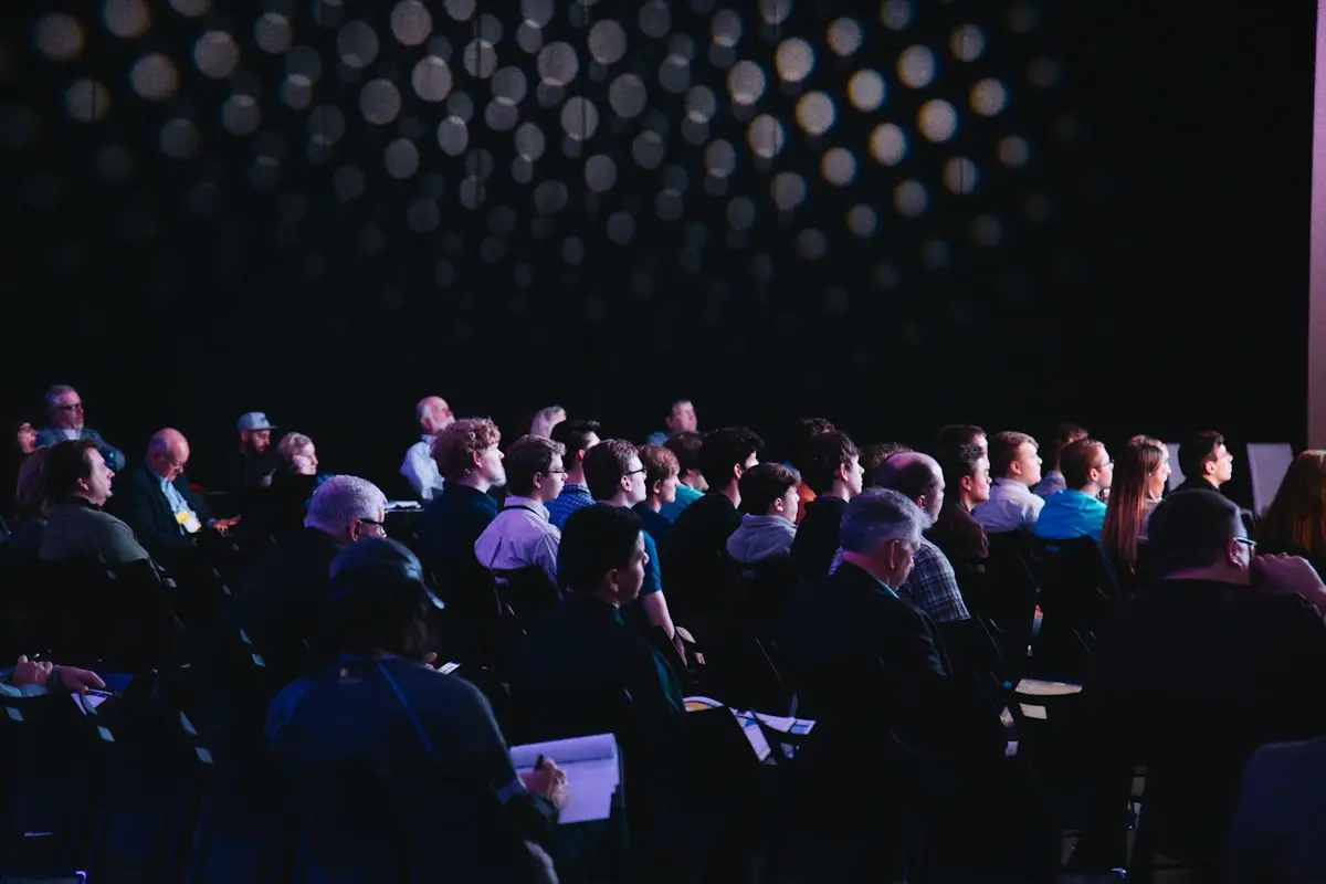 Seated audience filling a darkened auditorium, faces turned toward the stage