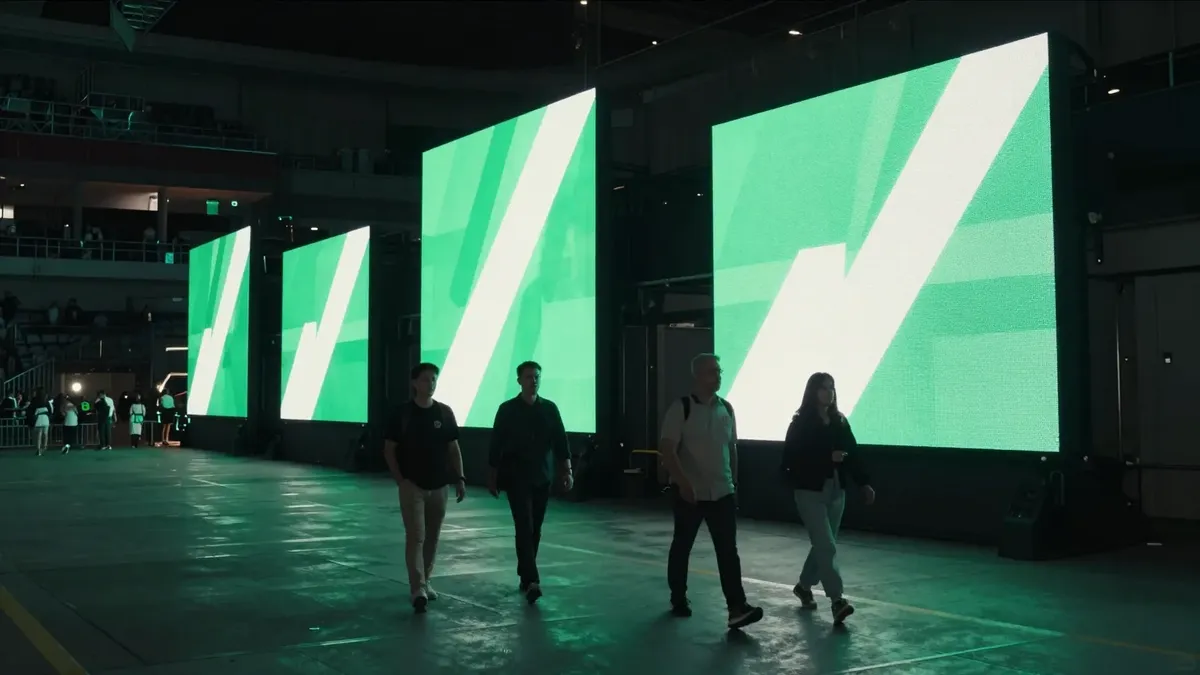 Fans walking through an arena concourse past tall illuminated LED sponsor boards