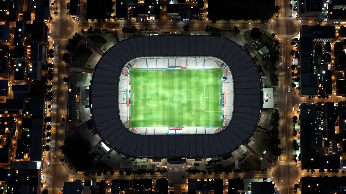 Night satellite view of a floodlit stadium surrounded by a lit city street grid